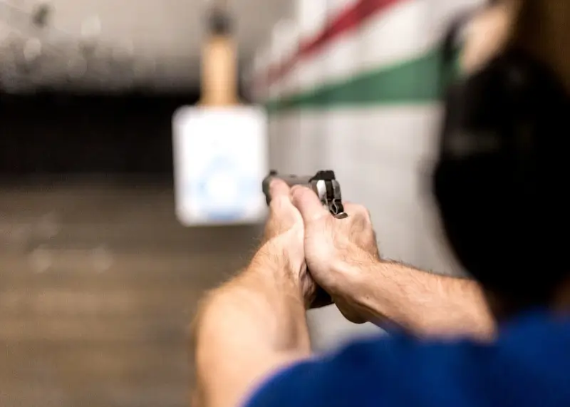 Close-up of hands holding and aiming a handgun toward a paper target at H&H shooting Sports range