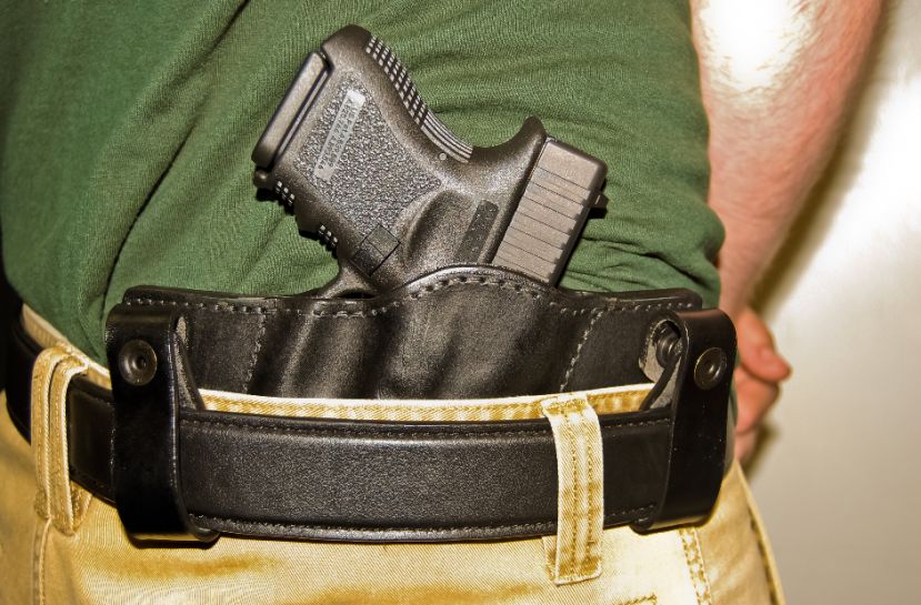 A firearm in a black leather holster clipped to a belt